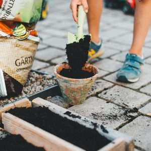 A child actively participates in gardening by shoveling soil into a pot on a patio.