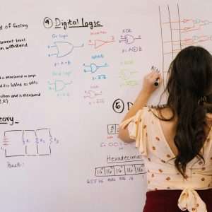 Female student writing circuit diagrams and logic gates in an educational setting on a whiteboard.