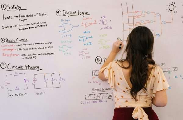 Female student writing circuit diagrams and logic gates in an educational setting on a whiteboard.