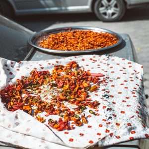 Dried chili peppers on fabric over a parked car under the sun.