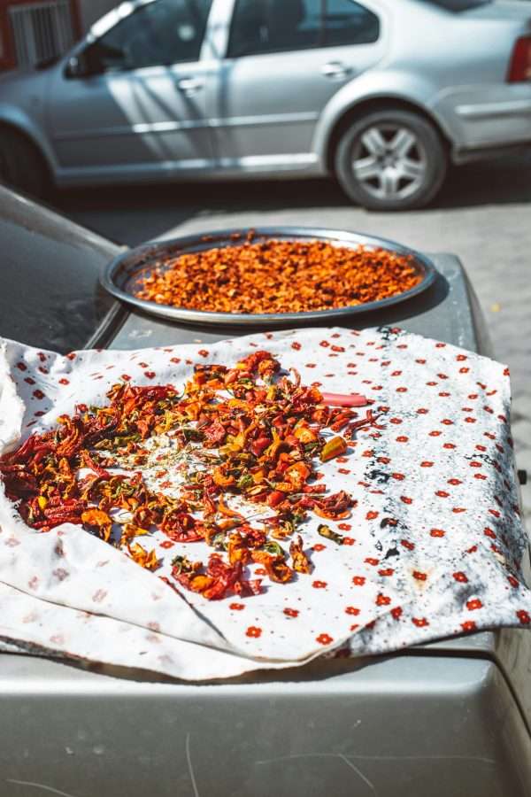 Dried chili peppers on fabric over a parked car under the sun.